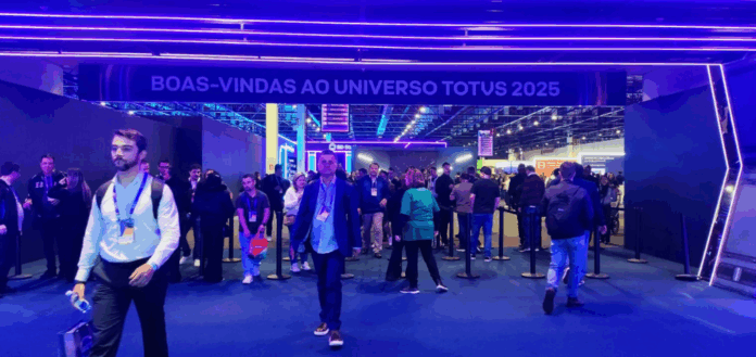 Universo TOTVS 2025 com participantes entrando sob letreiro de boas-vindas em ambiente iluminado com luzes roxas e azuis