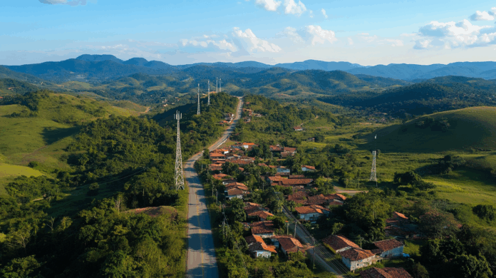 700 MHz: Vista aérea de áreas rurais brasileiras com sinal móvel se expandindo, incluindo torres de telecom, rodovias federais e pequenas comunidades conectadas.