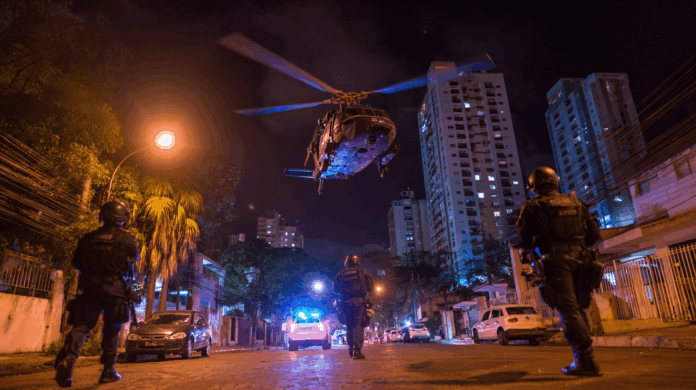 Helicóptero da polícia em perseguição após ataque hacker em São José, com viaturas em ação nas ruas e clima de operação de segurança.