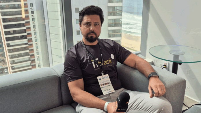 Resiliência cibernética sendo abordada por especialista da IT Brasil em entrevista no SecOps Meetup 2025, com vista para prédios e o mar ao fundo.